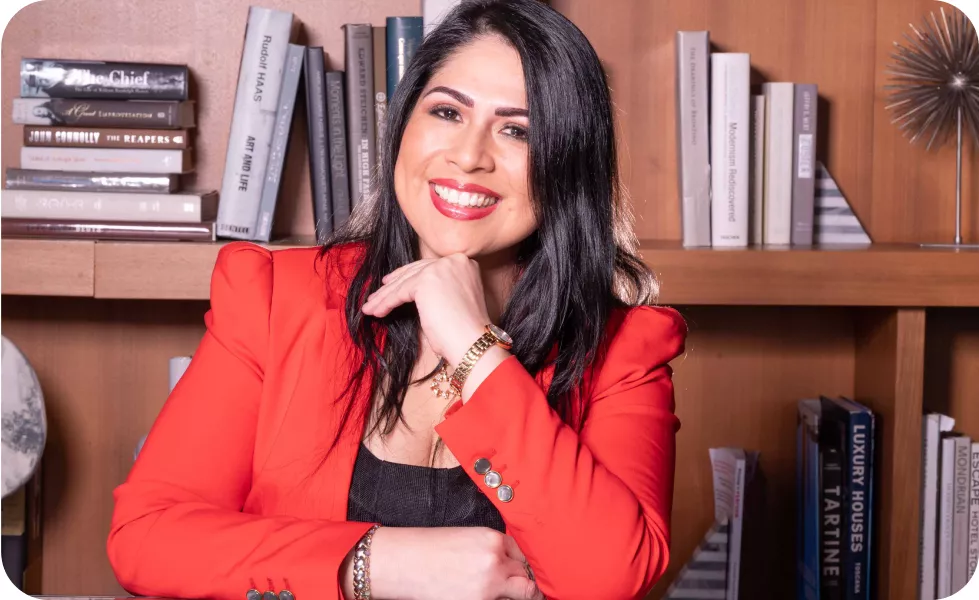 Magaly Ponce smiling confidently in a red blazer, seated with a hand resting on her chin.