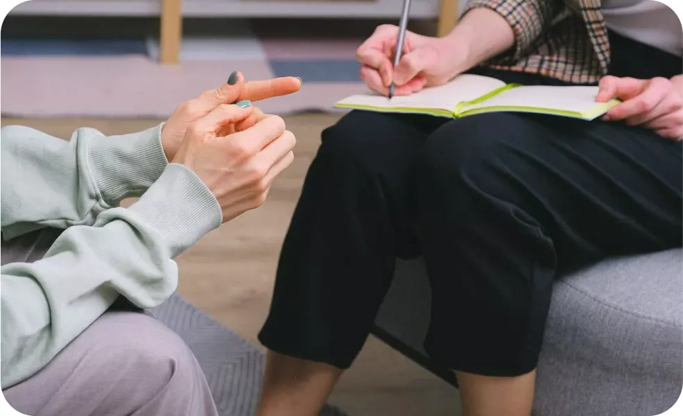 Close-up of two people in a conversation, one gesturing with their hand while the other writes in a notebook.